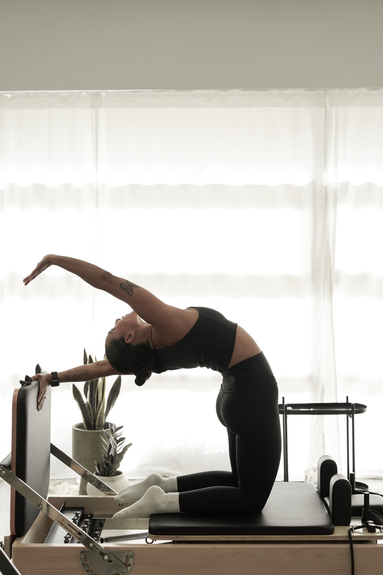 Alumna de MOVE en un estiramiento en arco sobre el Pilates Reformer, a contraluz en el estudio de Pozuelo